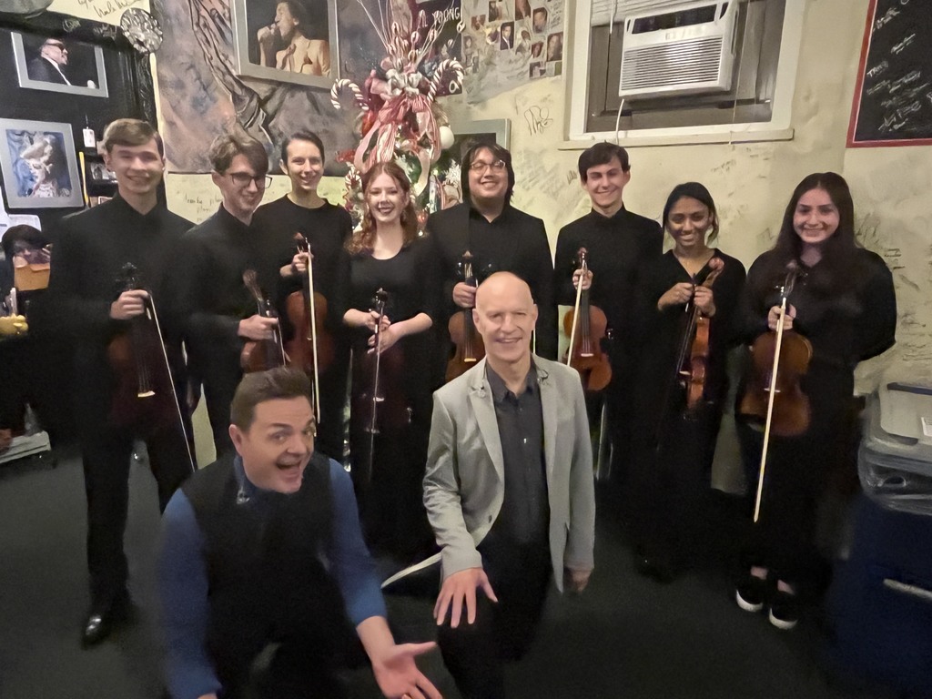 Back stage, student violinists pose in front of a Fox Theatre holiday tree with the Piano Guys.