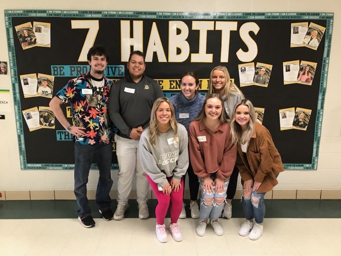 Seven of the FZE Leader in Me League posing in front of the 7 Habits bulletin board at St. Peters Elementary.