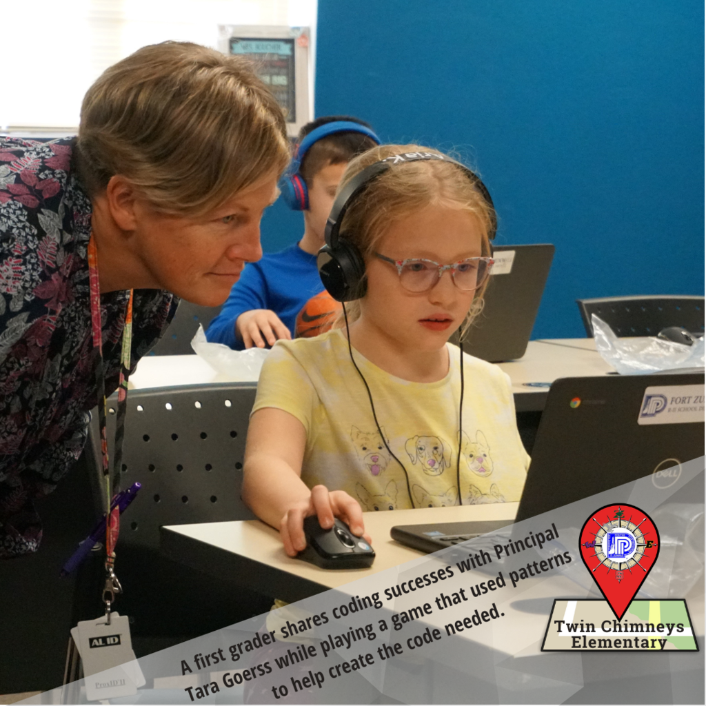 A first grader shares coding successes with Principal Tara Goerss while playign a game that used patterns to help create the code needed.