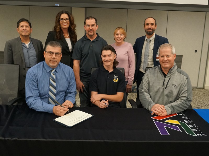 Hawbaker and his parents with USDOL officials, Zumwalt teachers and the CEO of Merric Millwork and Seating as he signs completion papers for his apprenticeship.