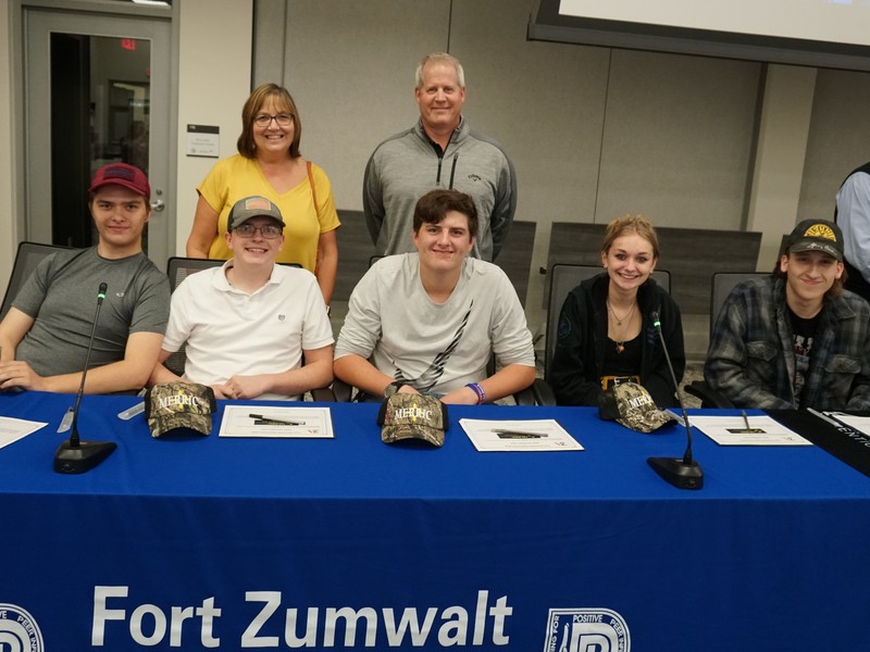 Merric Millwork and Seating officials pose at the signing table with their five new Zumwalt apprentices.